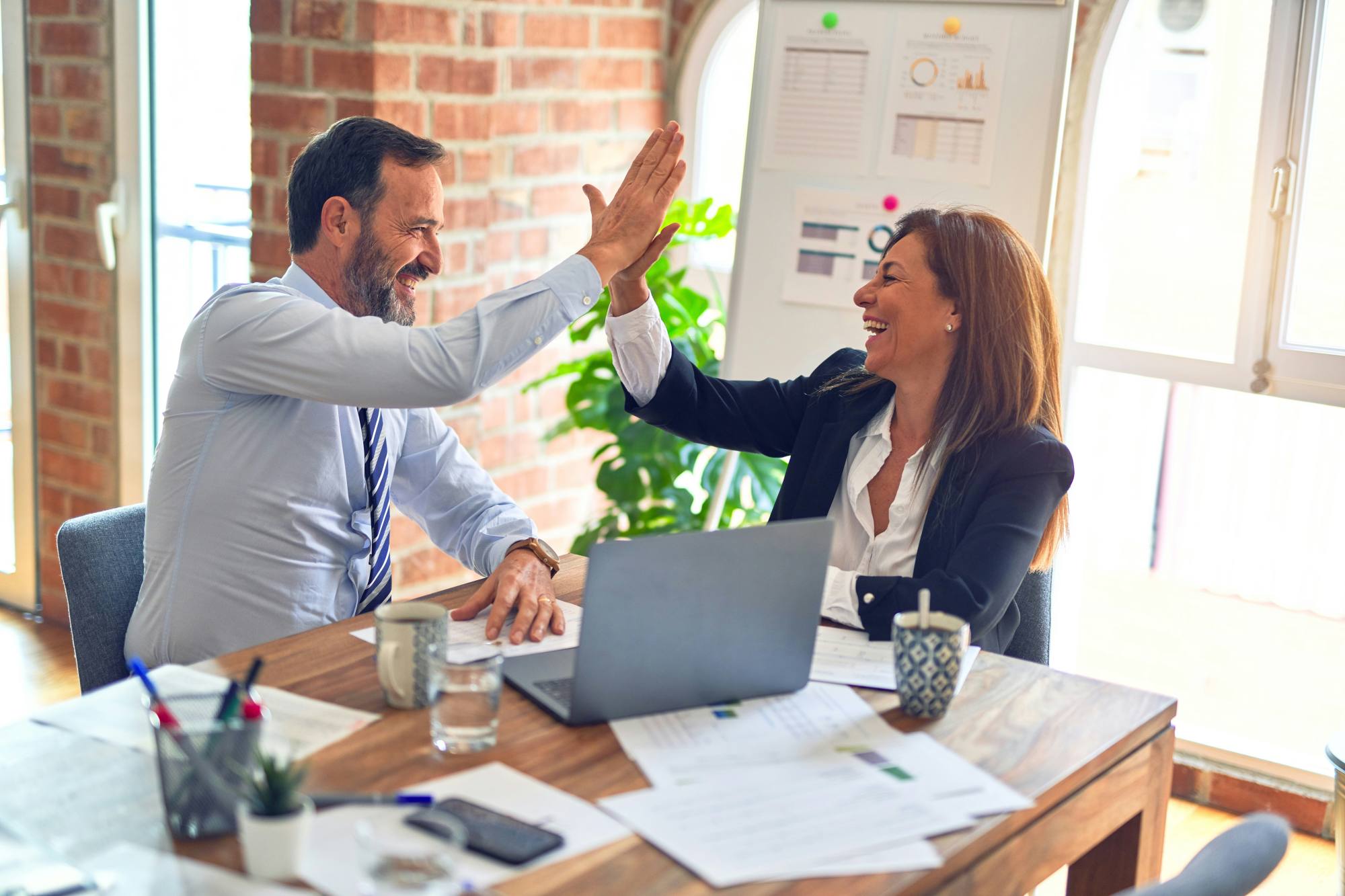 Twee collega’s geven elkaar een high five aan een vergadertafel